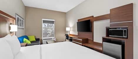 A hotel room with a large bed, a desk with a chair, a television, a microwave, and a refrigerator.