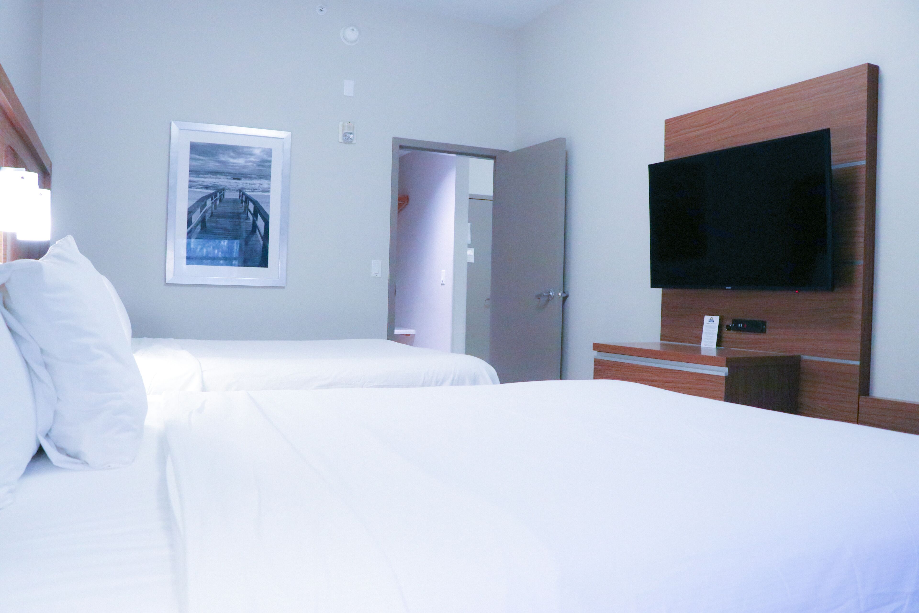 A hotel room with two beds, a flat-screen TV mounted on the wall, and a framed picture on the wall.