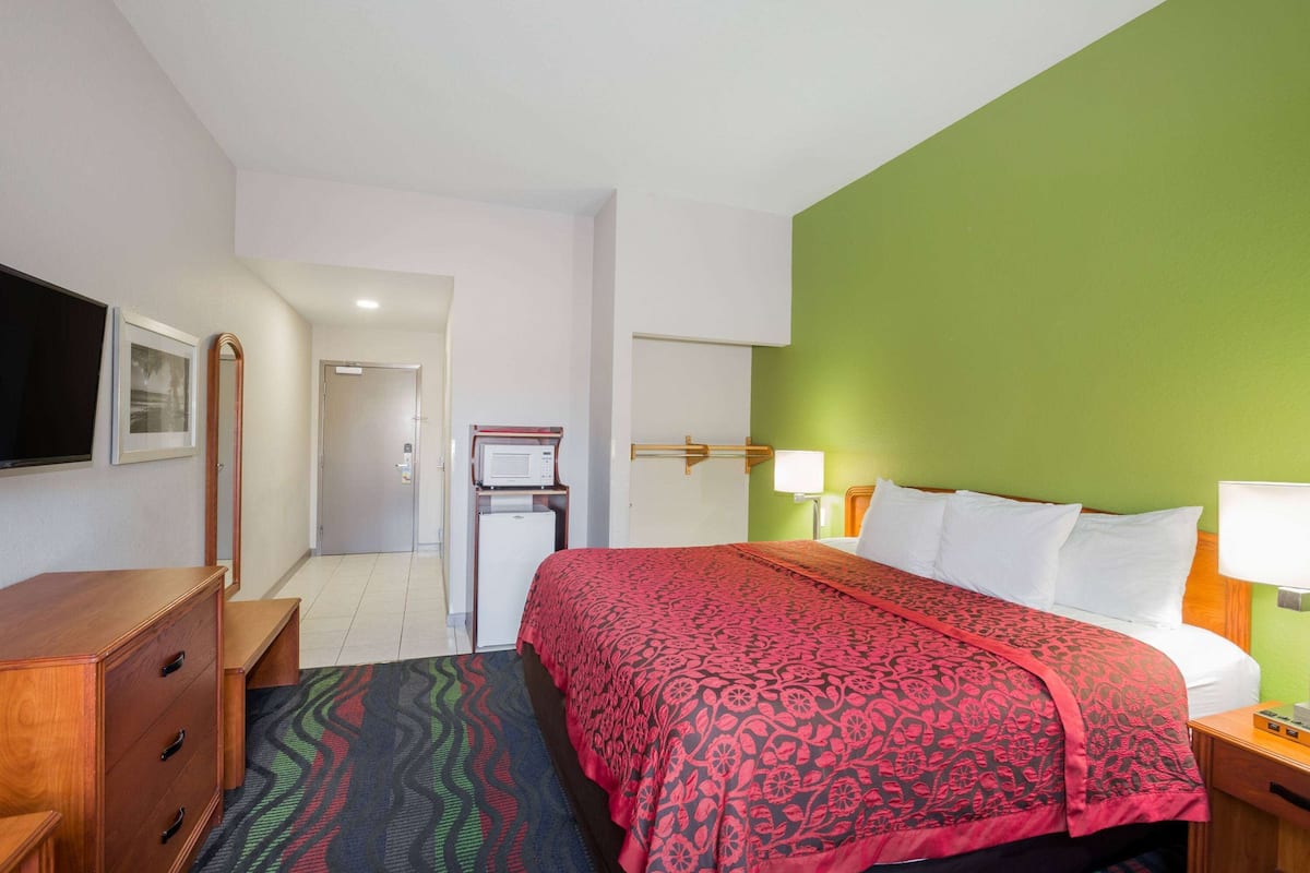 Une chambre d’hôtel comprenant un lit, une commode, un bureau, une télévision et une porte donnant sur une autre pièce.