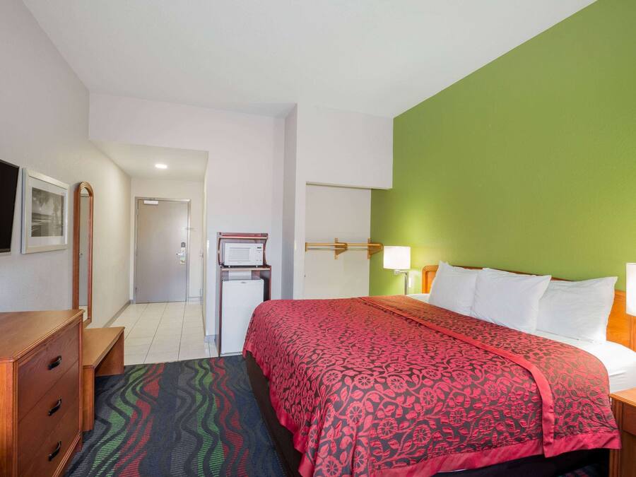 A hotel room with a bed, a dresser, a desk, a television, and a door leading to another room.