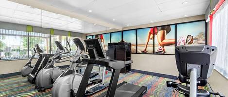 A gym with treadmills, ellipticals, and a stationary bike, featuring large windows and motivational posters.