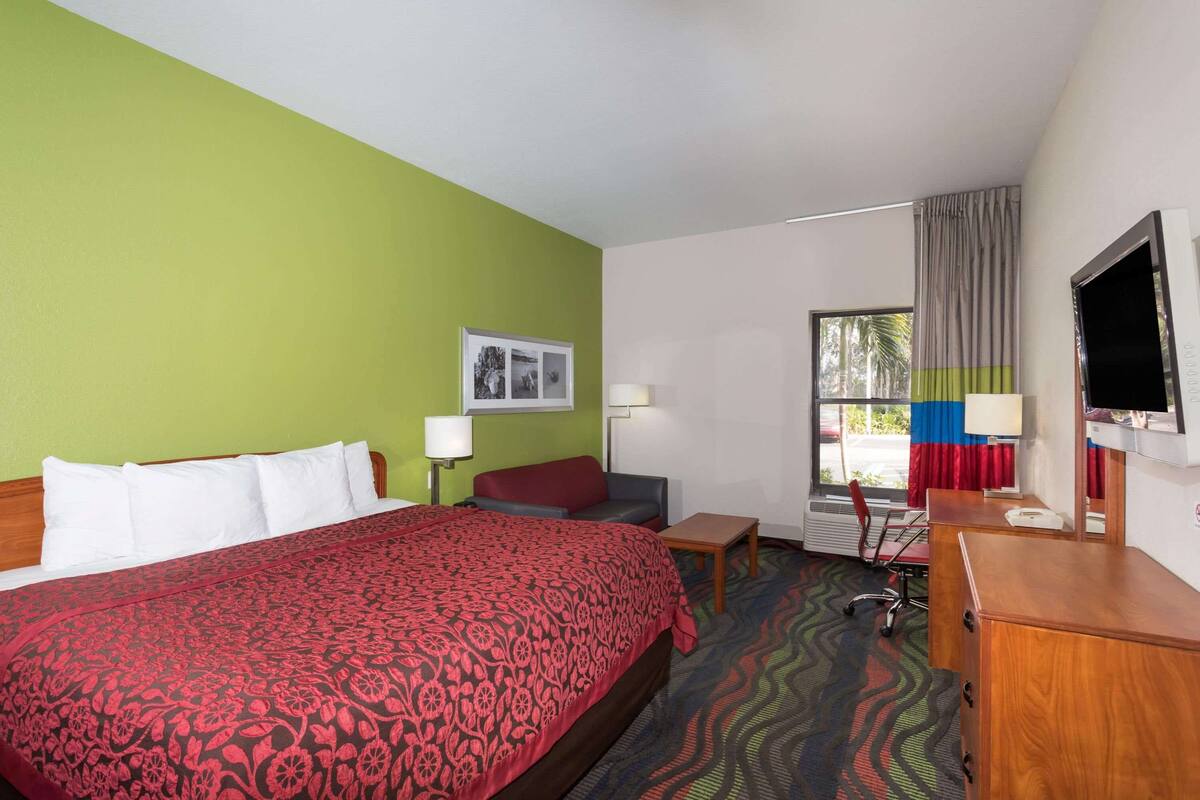 Une chambre d’hôtel avec un grand lit, un bureau, une chaise, une télévision et une fenêtre avec des rideaux.
