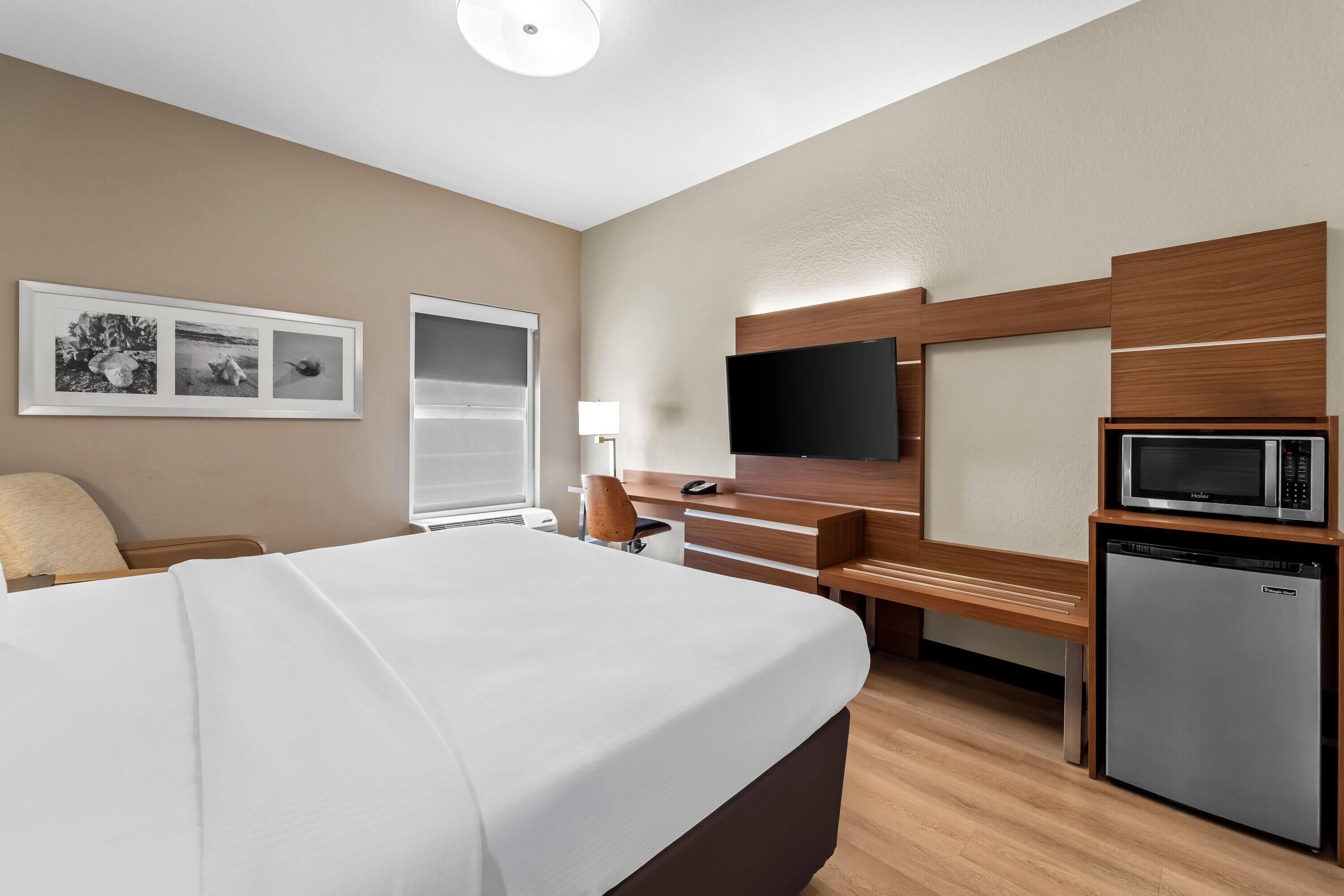 A hotel room with a bed, a desk, a television, a microwave, and a refrigerator.