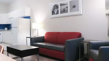 A compact living space with a kitchenette, a red sofa, a small table, and a framed picture on the wall.