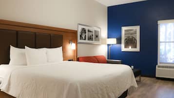 Habitación de hotel con una cama grande, cabecera de madera, mesita de noche, una silla roja, una lámpara de pared y dos cuadros enmarcados.