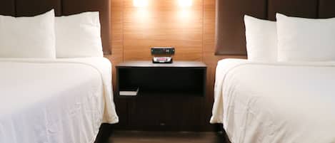 A hotel room with two beds, a nightstand with a clock, and a wooden headboard.