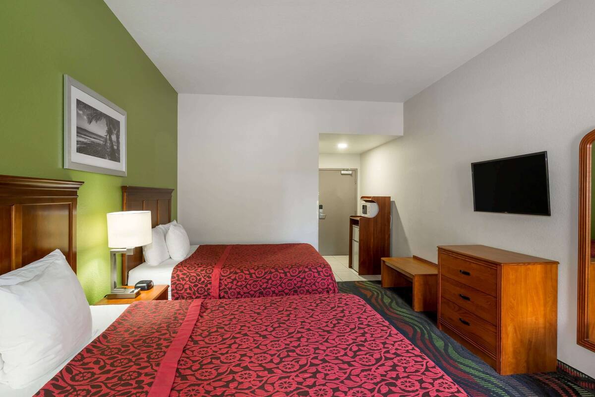 Une chambre d’hôtel avec deux lits, un bureau, une commode, une télévision et un tableau encadré au mur.
