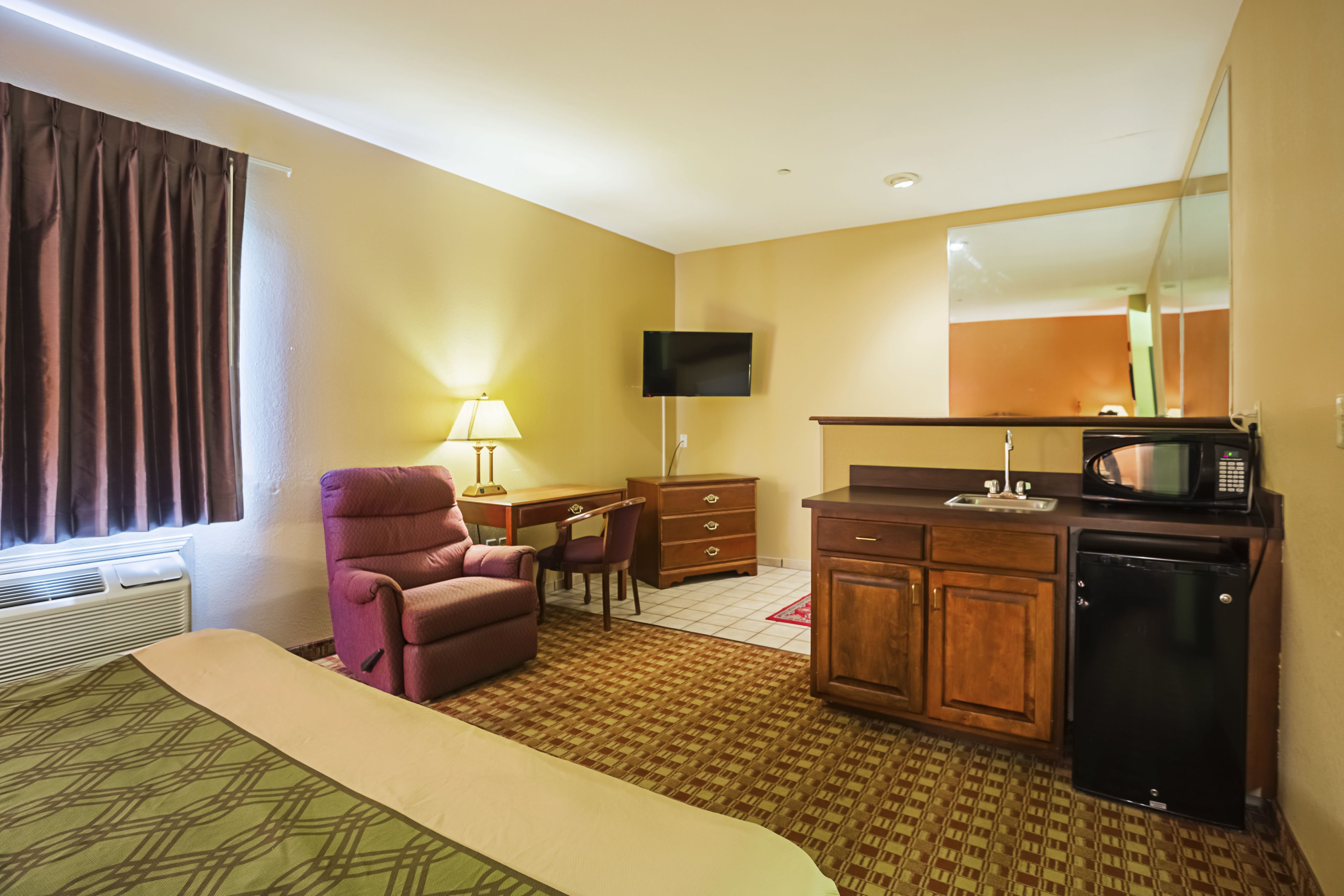 Una habitación de hotel con cama, escritorio, silla, televisor, microondas y refrigerador.