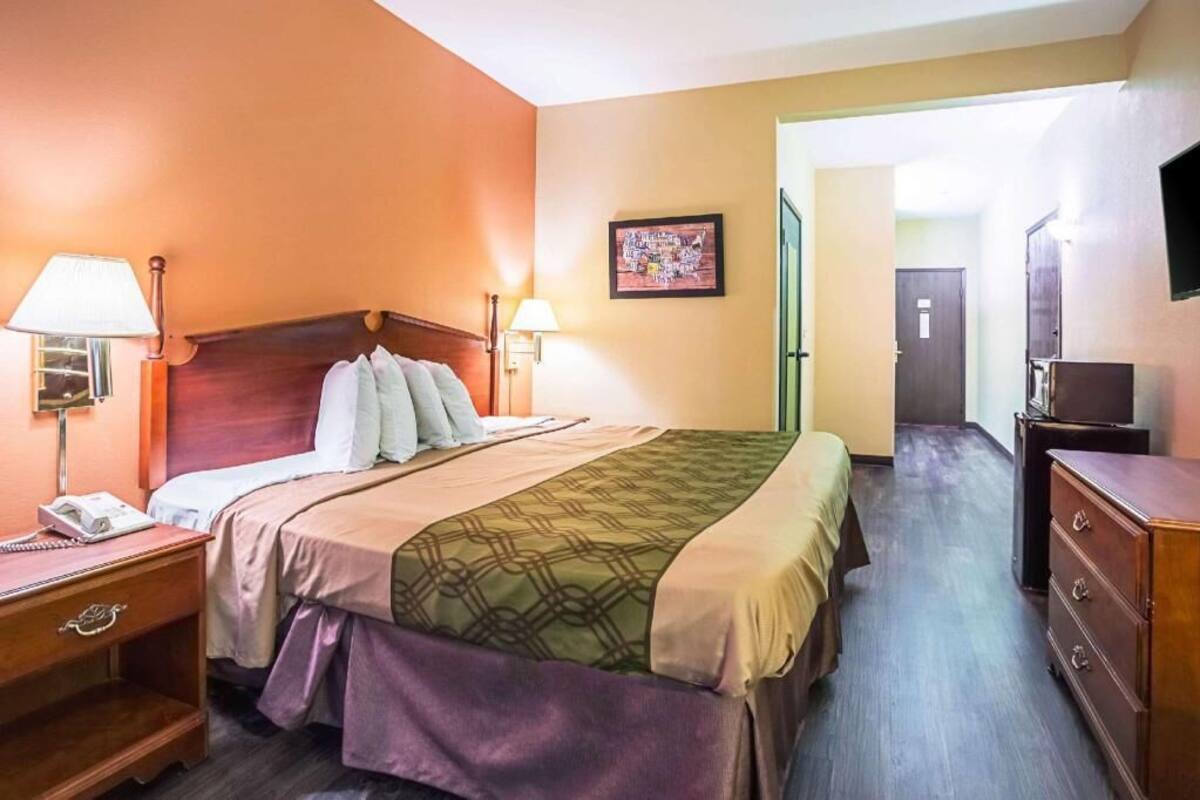 A hotel room with a bed, bedside lamps, a dresser, and a television.