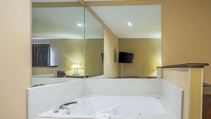 A bathroom with a large mirror, a bathtub, a sink, and a television mounted on the wall.