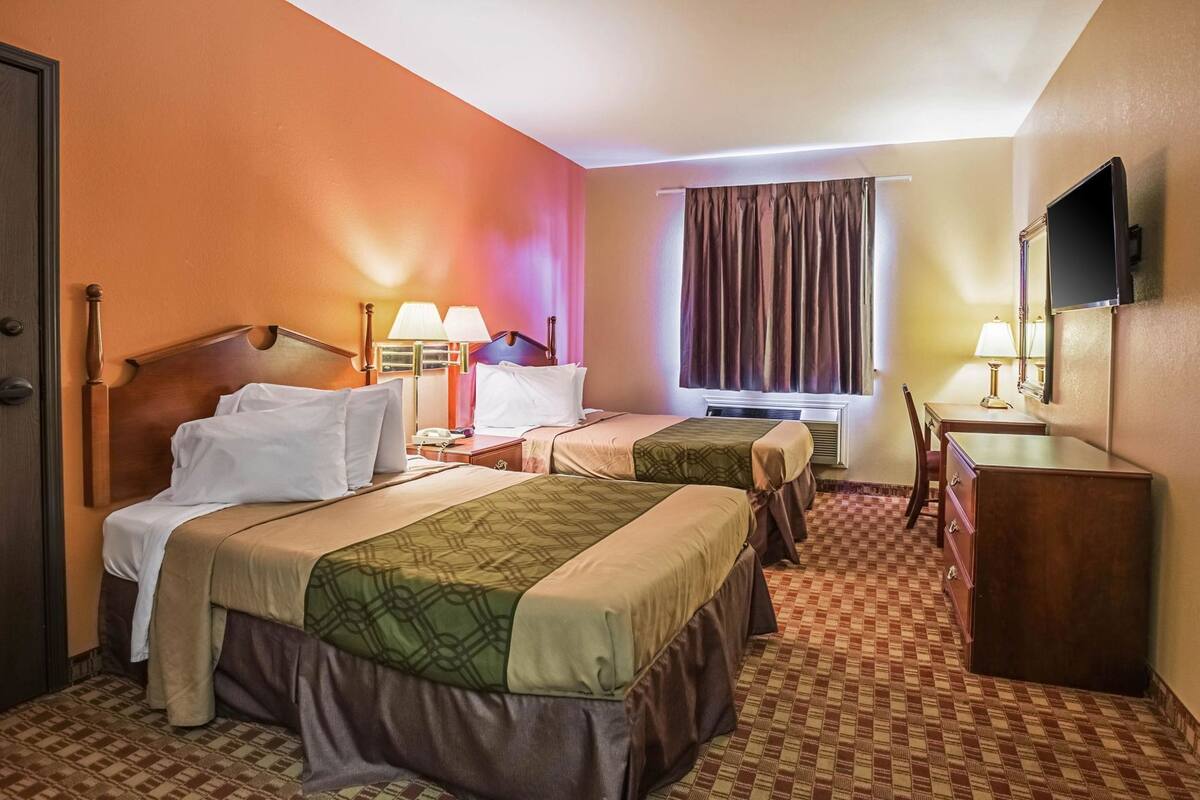 A hotel room with two beds, a desk, a chair, a TV, and a window with curtains.