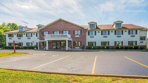 A two-story hotel with a central entrance, a covered porch, and a parking lot in front.
