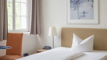 A hotel room with a bed, a chair, a nightstand with a lamp, a phone, and a window with curtains.