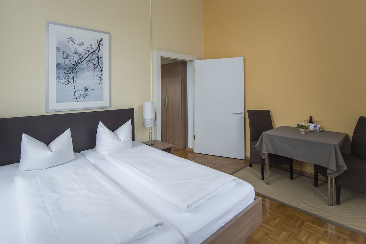 A hotel room with a large bed, a desk with a chair, a door, and a framed picture on the wall.
