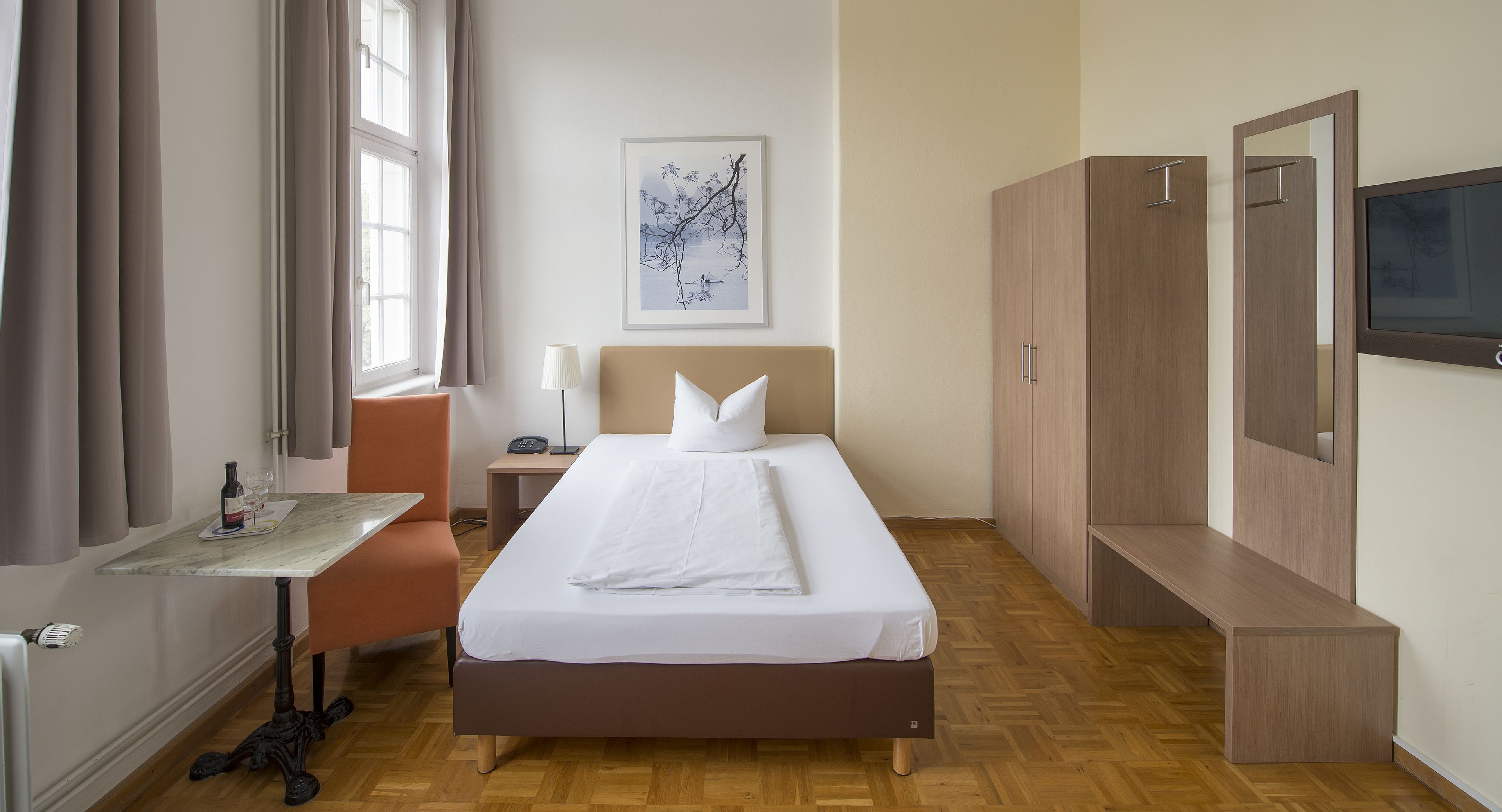 A hotel room with a bed, bedside table, lamp, and a painting on the wall.