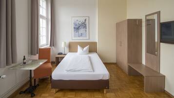 A hotel room with a bed, bedside table, lamp, and a painting on the wall.