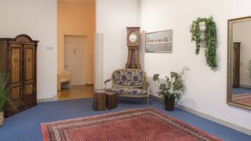A room with a wooden wardrobe, a blue armchair, a clock, a potted plant, and a mirror on the wall.