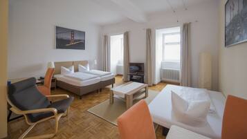 A hotel room with two beds, a desk, a chair, a TV, and a large window with curtains.