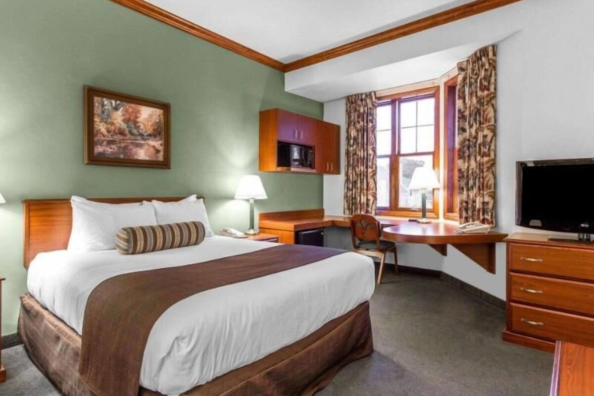 A hotel room with a bed, desk, chair, television, and a painting on the wall.