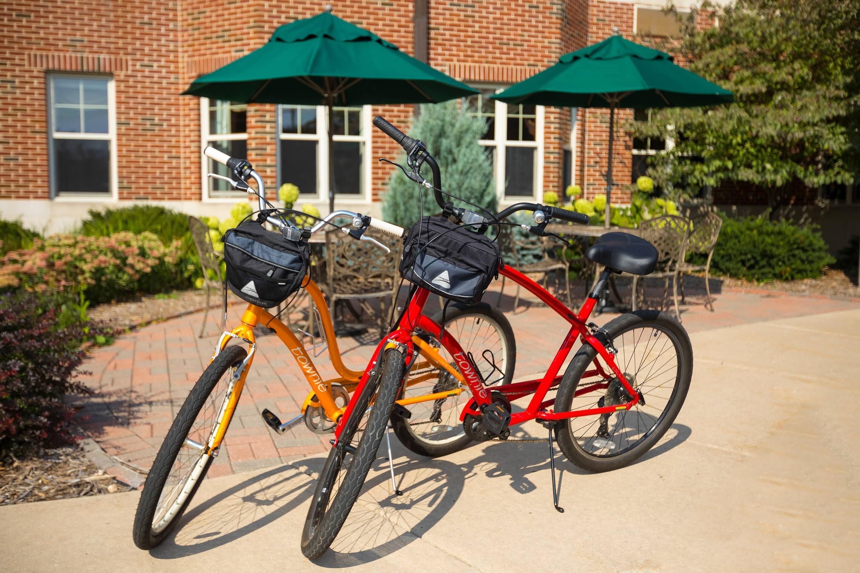 Two bicycles parked in front of a building with brick walls and green umbrellas.