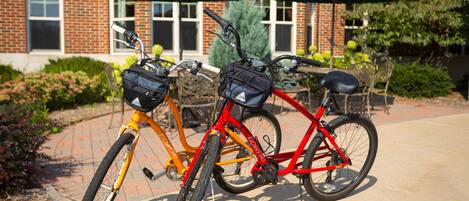 Two bicycles parked in front of a building with brick walls and green umbrellas.