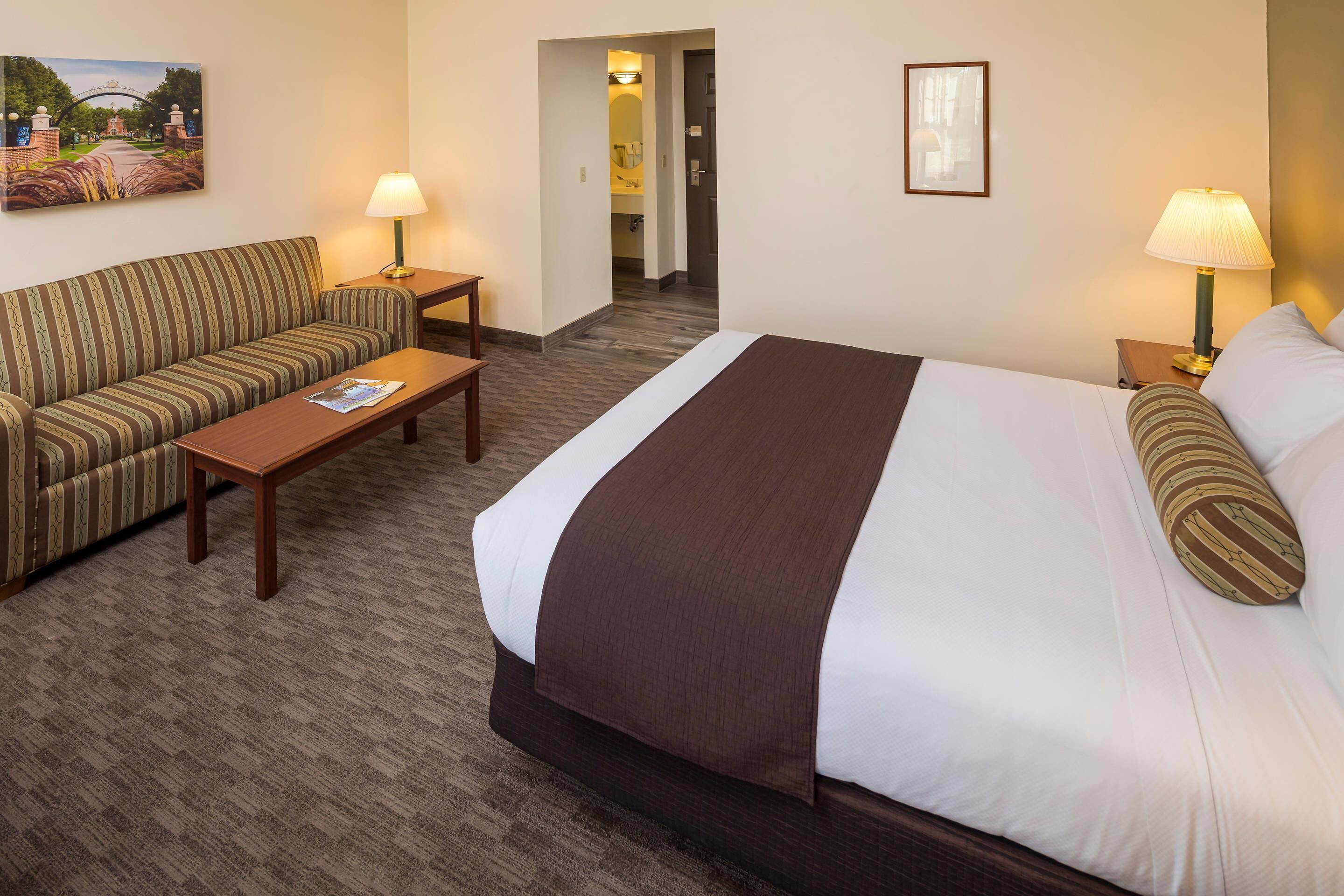 A hotel room with a large bed, a sofa, a small table, and two lamps.