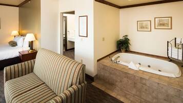 A hotel room with a bed, a striped sofa, a large bathtub, and a small potted plant.