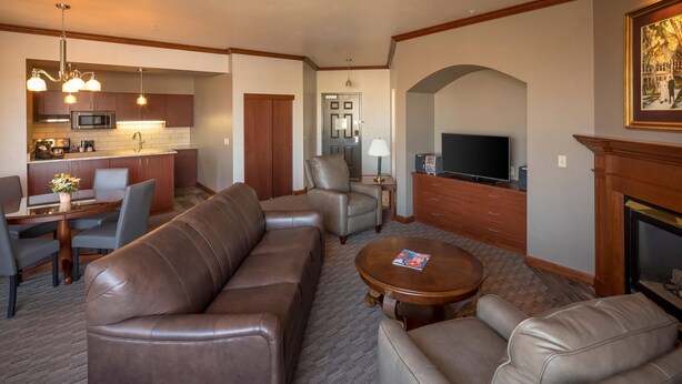 A spacious living room with a brown leather sofa, a coffee table, and a TV. There is a kitchen area with a microwave and cabinets. - Kress Inn, an Ascend Collection Hotel (De Pere)