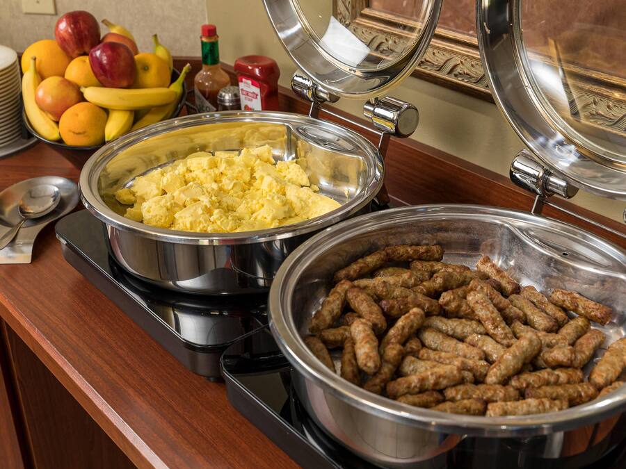 A buffet with various food items including sausages, scrambled eggs, and fruits.