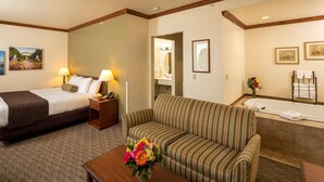A hotel room with a bed, a sofa, a small table with a vase of flowers, a bathroom with a bathtub, and a mirror. - Kress Inn, an Ascend Collection Hotel (De Pere)