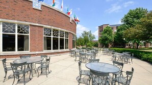 A brick building with large windows and multiple flags. Outside, there are round tables and chairs arranged on a patio. - Kress Inn, an Ascend Collection Hotel (De Pere)