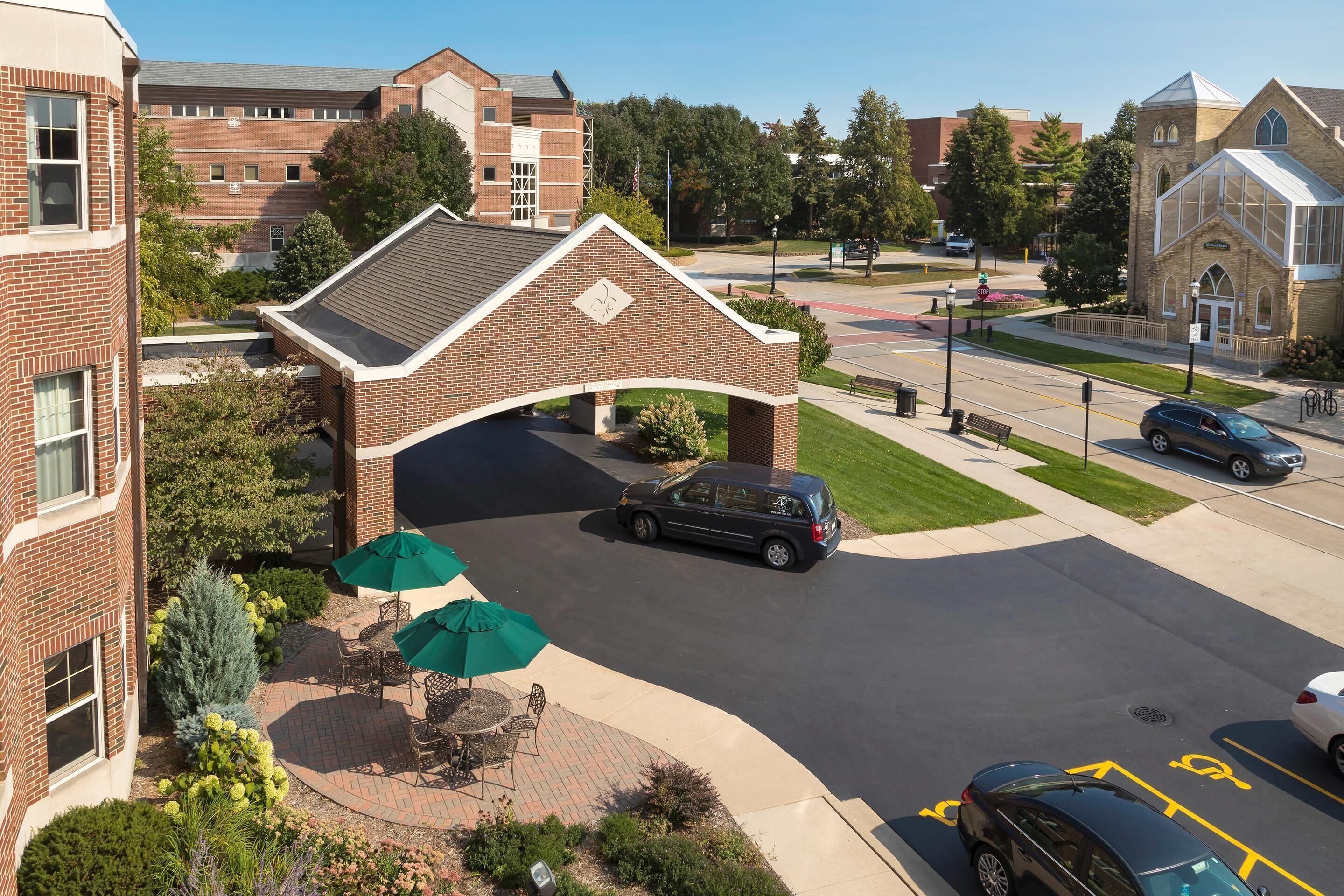 A parking area with a covered walkway, a car, and a building with a brick facade.