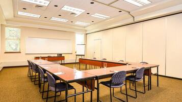 A conference room with a long table, chairs, a whiteboard, and a projector screen.
