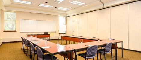 A conference room with a long table, chairs, a whiteboard, and a projector screen.
