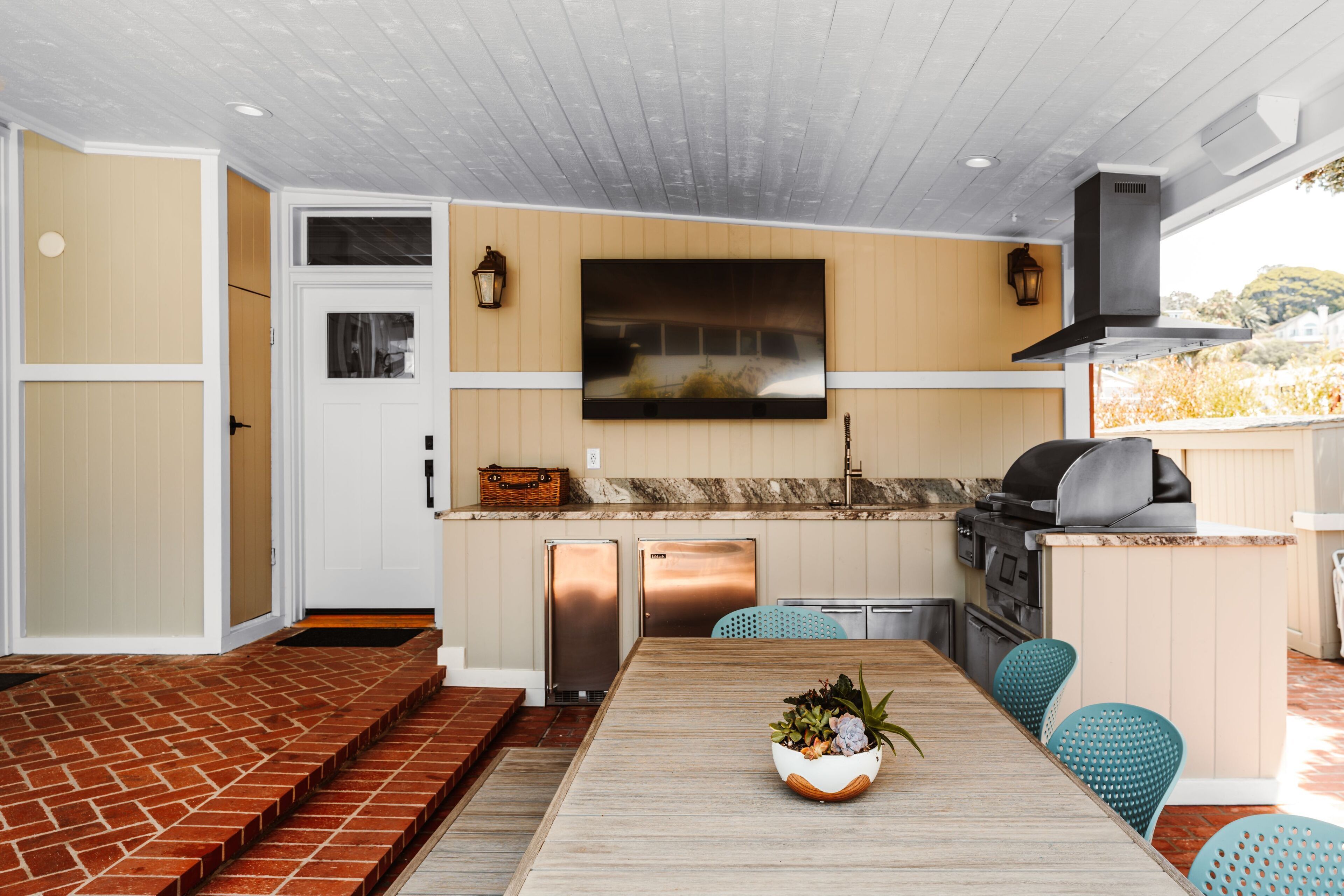 A modern kitchen with a flat-screen TV, built-in appliances, and a dining area with a wooden table and blue chairs.