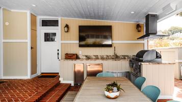 A modern kitchen with a flat-screen TV, built-in appliances, and a dining area with a wooden table and blue chairs.