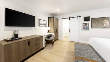 A modern hotel room with a large bed, a desk with a coffee maker, a chair, and artwork on the walls.