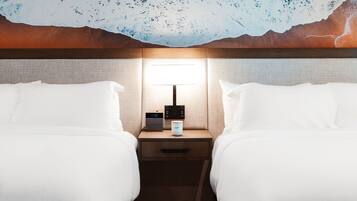 Een hotelkamer met twee bedden, een nachtkastje met een klok en een koffiezetapparaat, en een muurschildering.