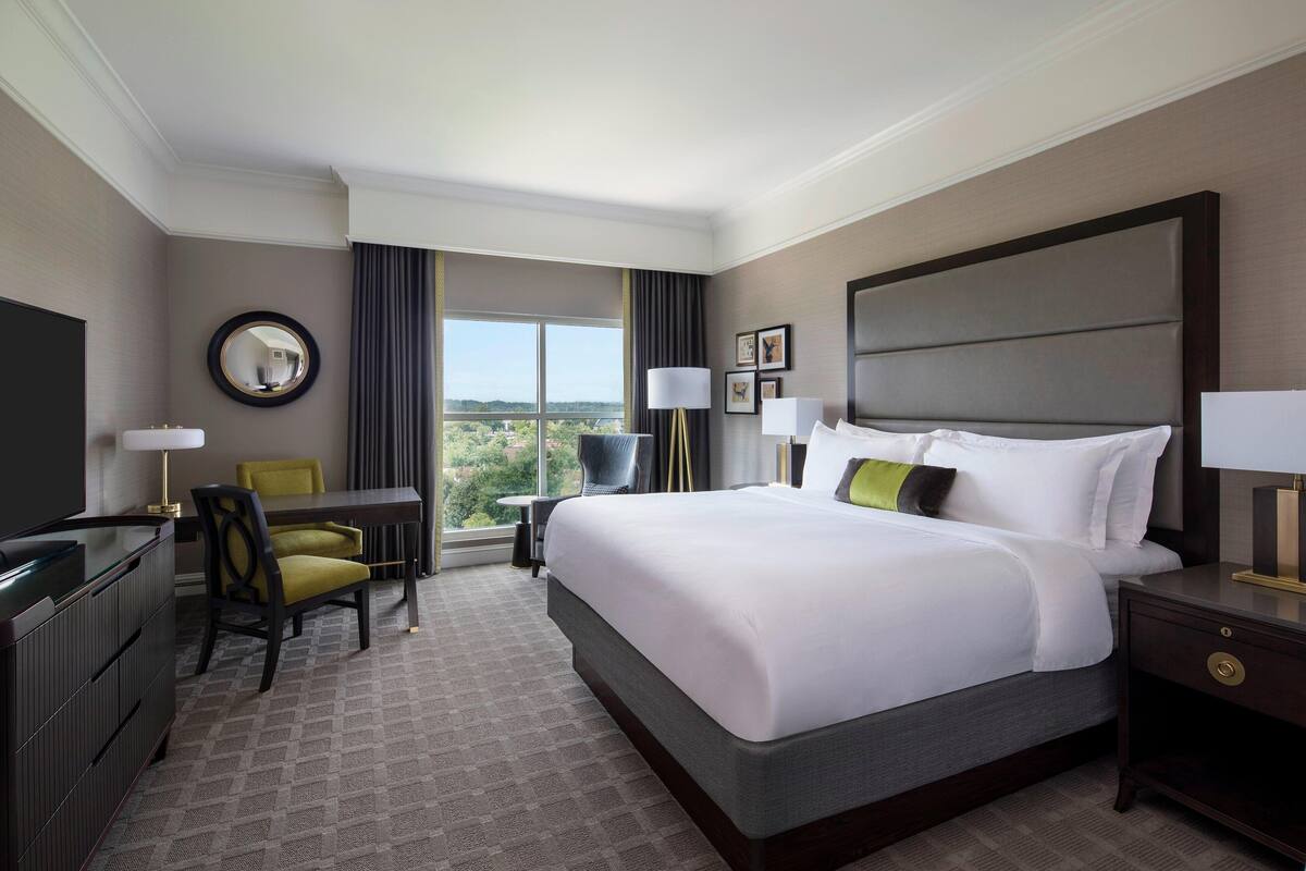 Une chambre d’hôtel avec un grand lit, un bureau avec une chaise, une télévision et une vue sur l’extérieur.
