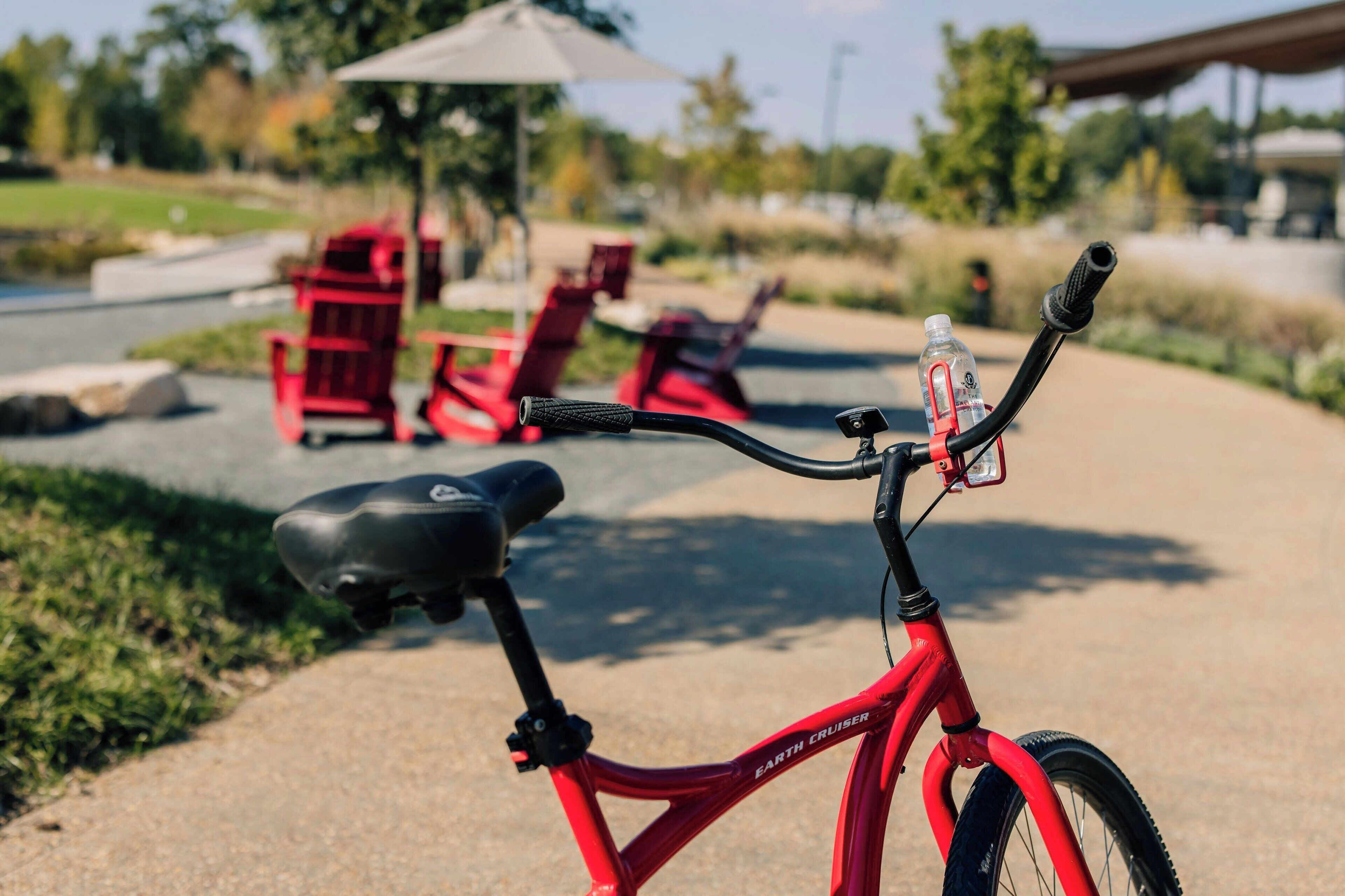 A red bicycle with a water bottle and a black seat, parked on a paved path.