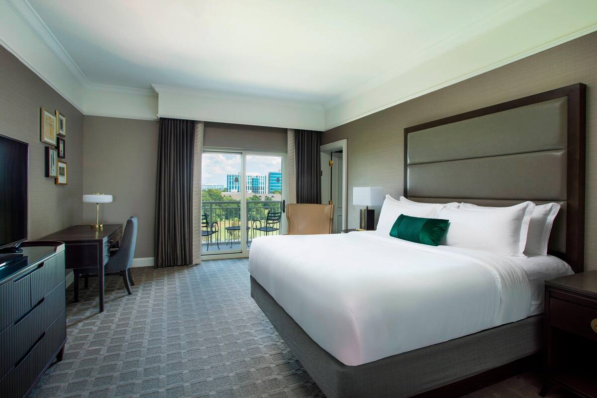 Une chambre d’hôtel avec un grand lit, un bureau avec une chaise, une télévision et une vue sur l’extérieur grâce à une grande fenêtre.