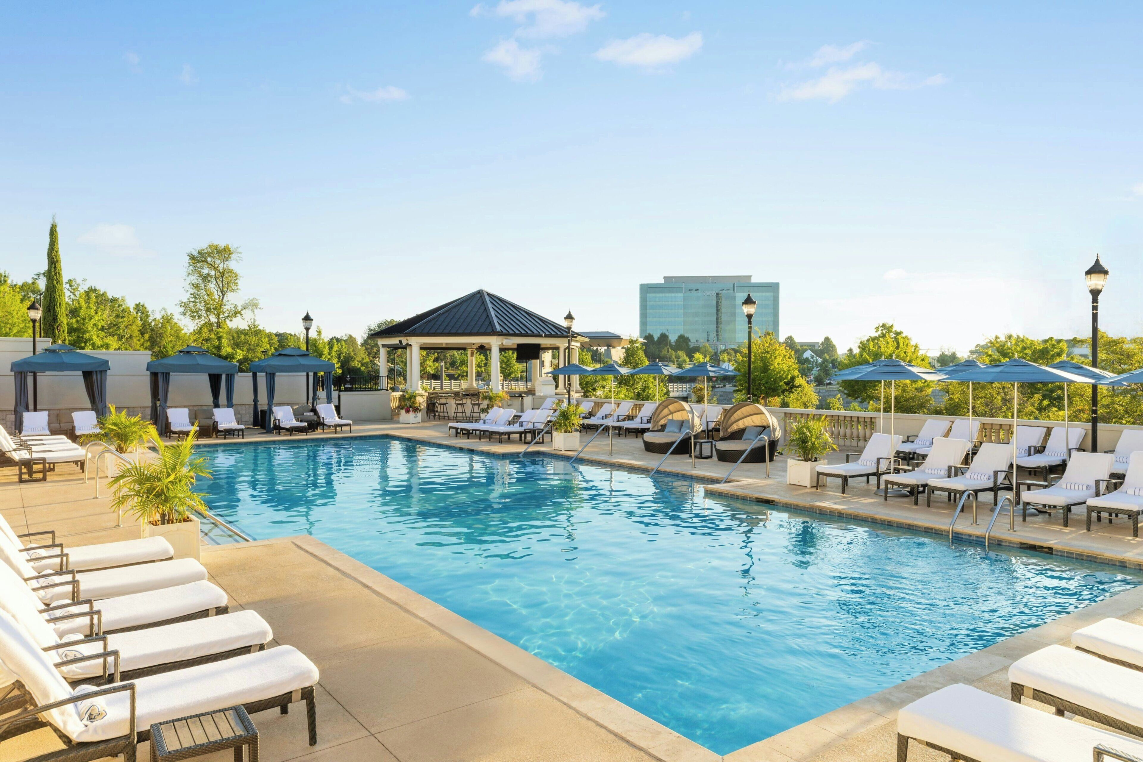 A pool area with lounge chairs and umbrellas, a gazebo, and a modern building in the background.