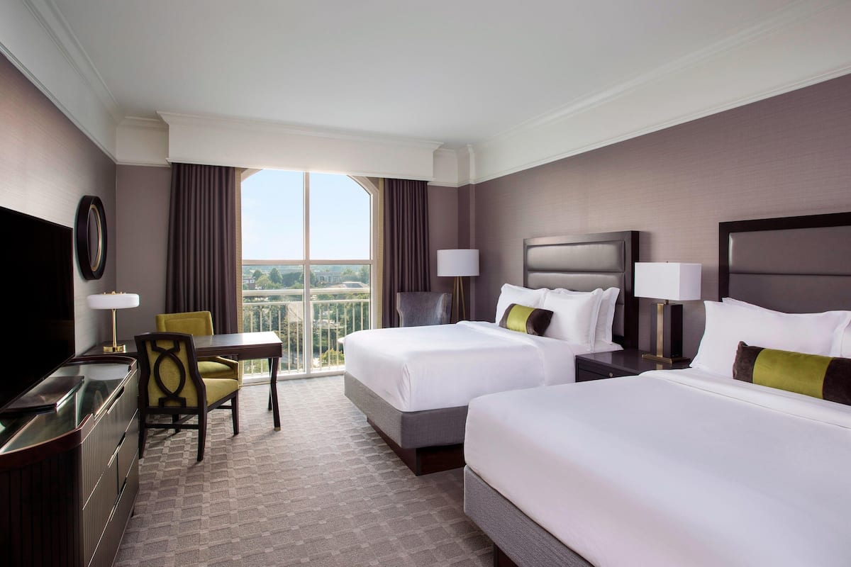 Une chambre d’hôtel avec deux lits, un bureau avec une chaise, une télévision et une grande fenêtre donnant sur la ville.
