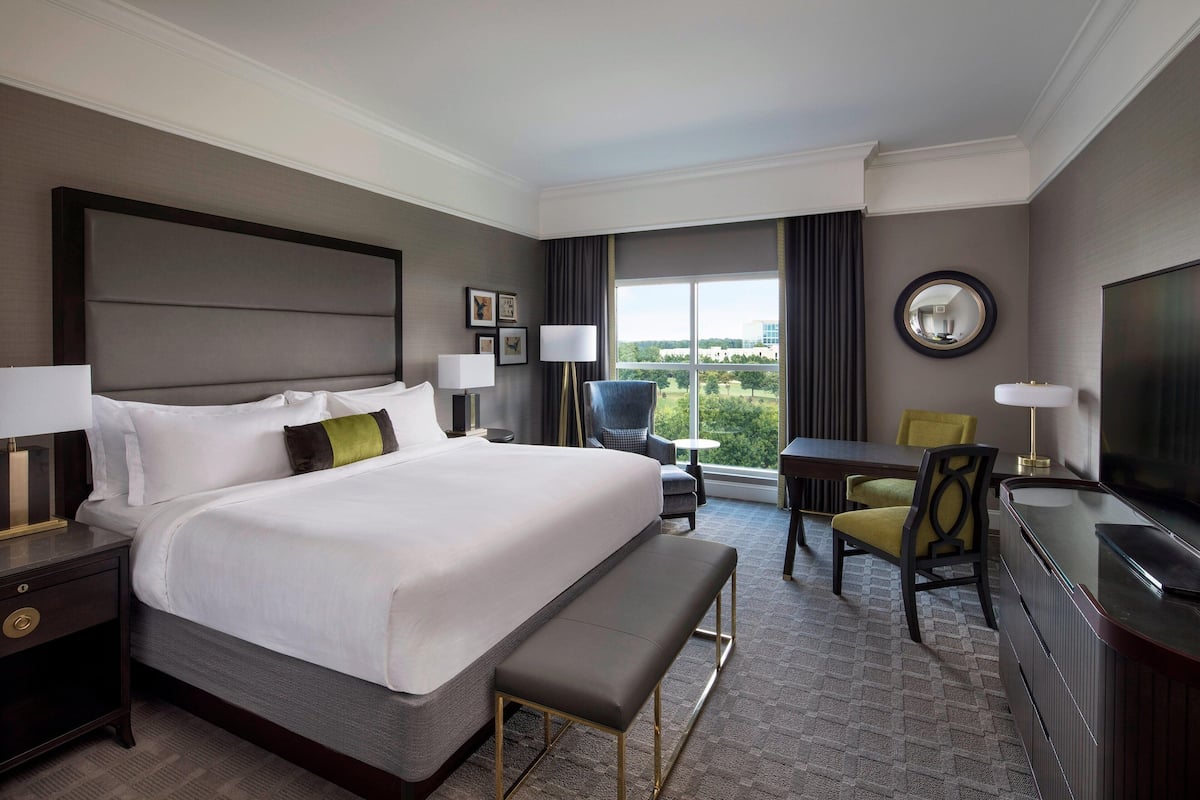 Une chambre d’hôtel avec un grand lit, un bureau, une chaise, un banc, une télévision et une fenêtre donnant sur un beau paysage.