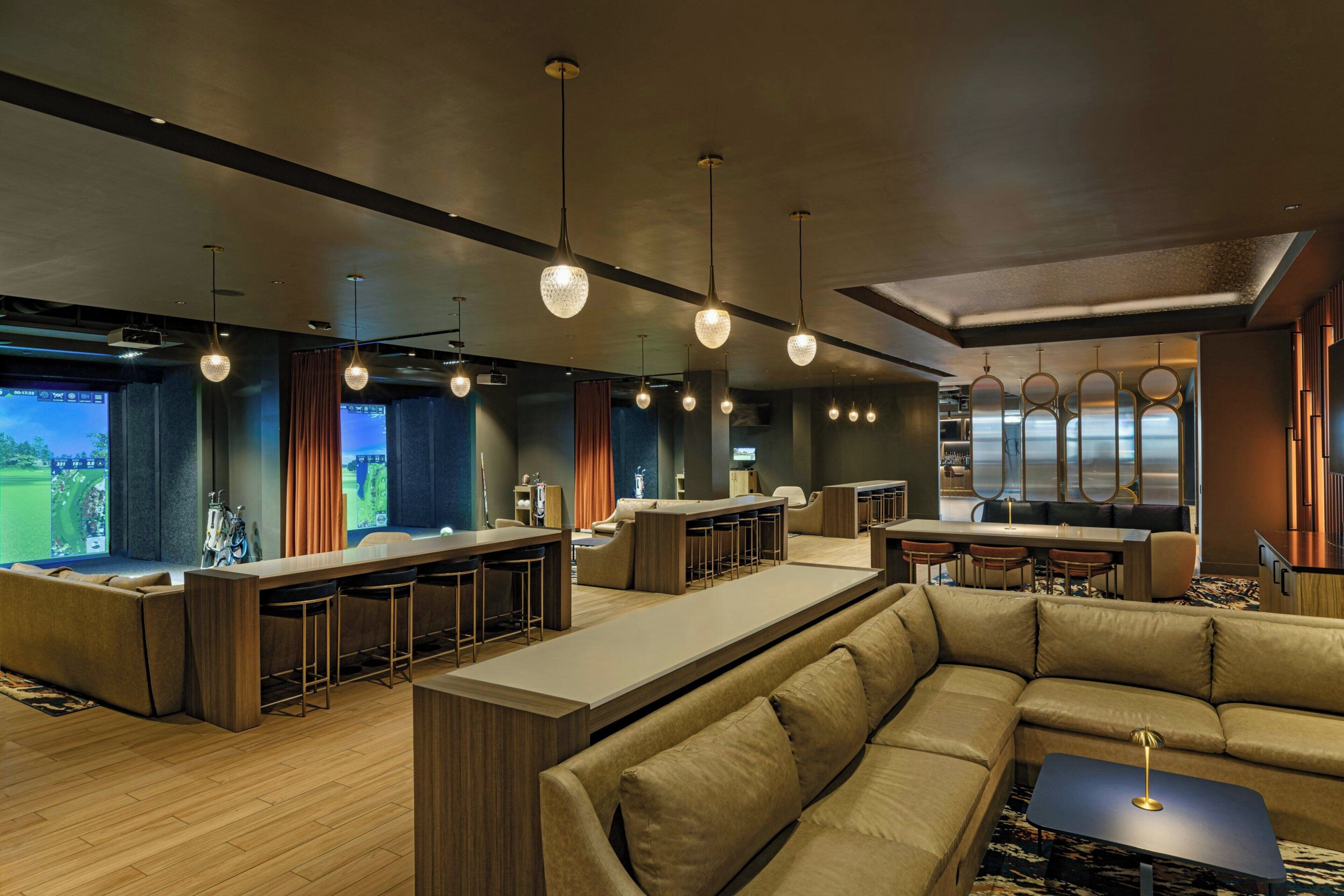 A modern bar area with a long counter, multiple stools, and overhead lighting.