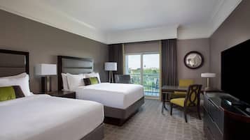 A hotel room with two beds, a desk with a chair, a television, and a balcony with a view.
