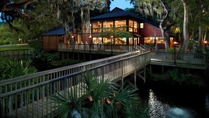 A waterfront property with a wooden deck, a dining area, and a building with large windows.