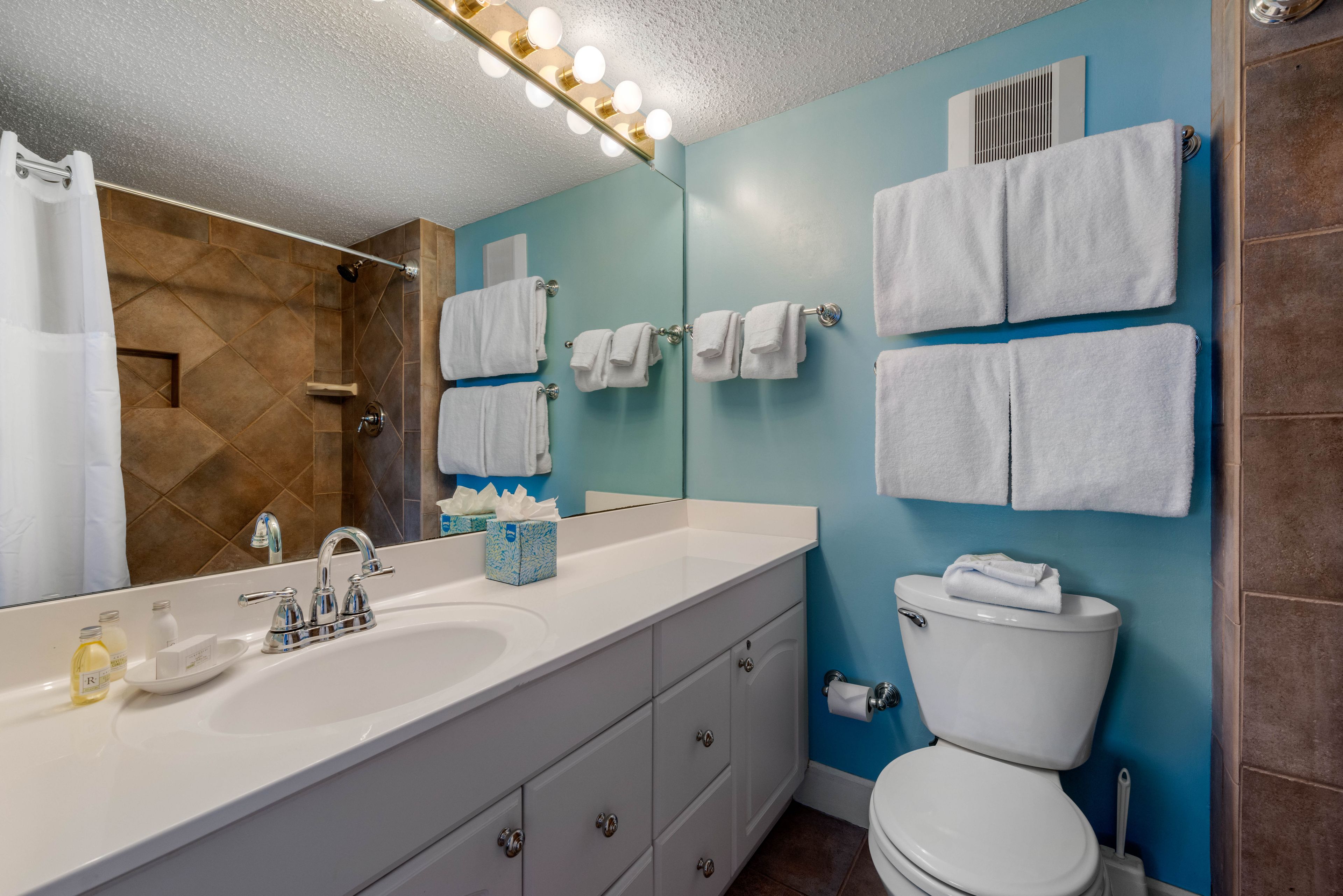 A bathroom with a white sink, a mirror, a toilet, and towels hanging on the wall.