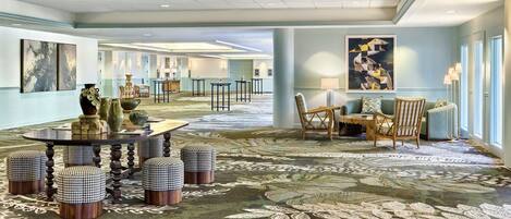 A spacious lobby with a round table, checkered ottomans, and a patterned carpet.