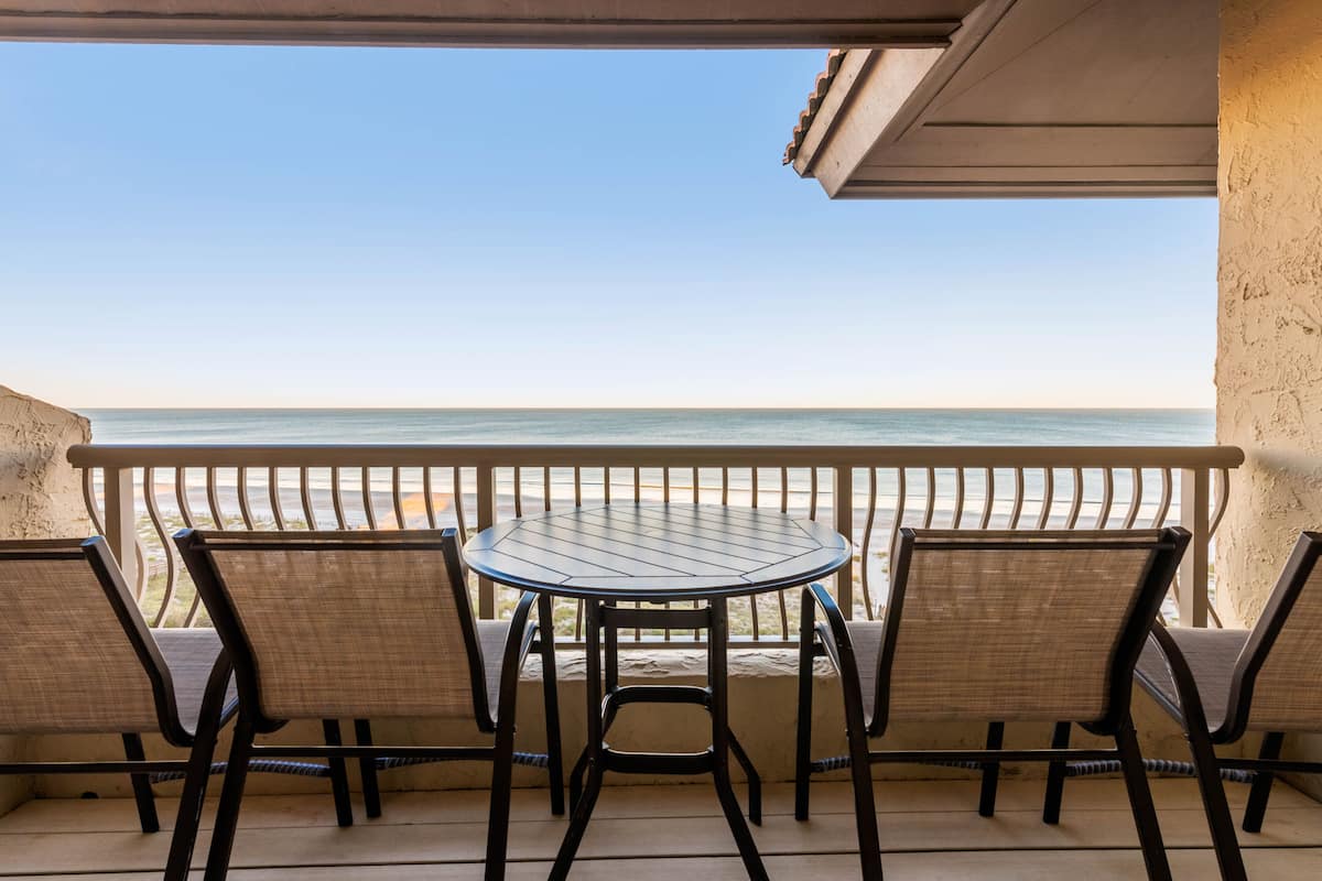 A balcony with a table and chairs overlooking a beach.